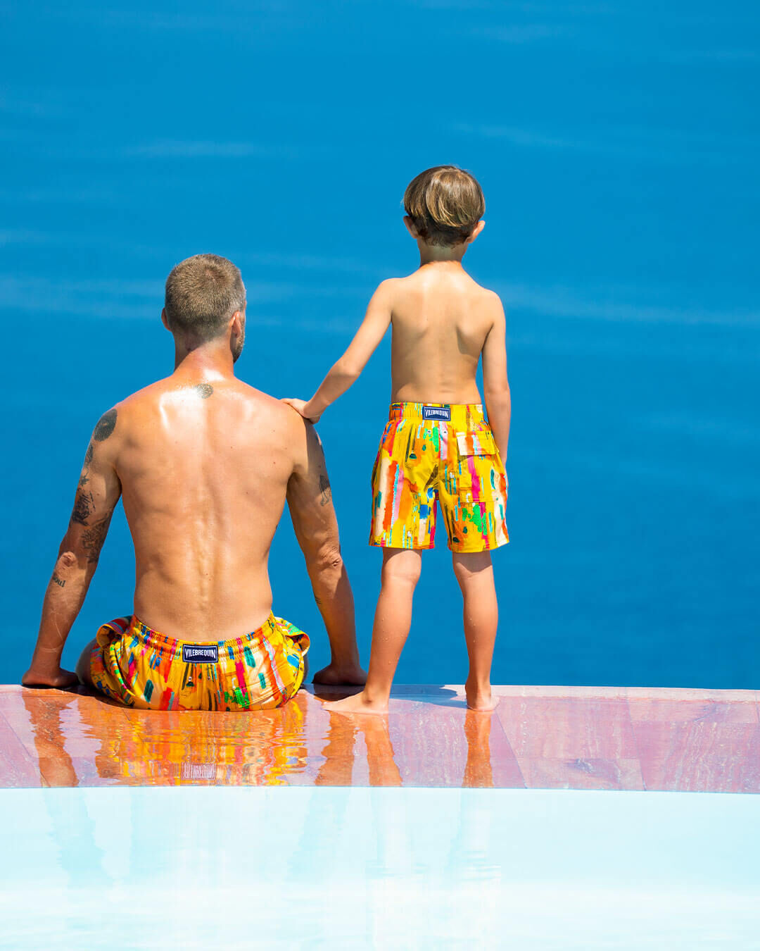 A man and a boy from behind sitting next to each other looking at the sea